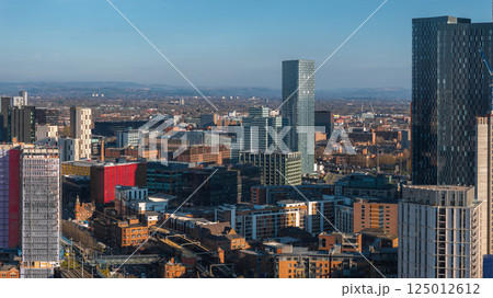 Aerial view of Manchester, UK, showcasing modern skyscrapers, mixed architecture, and rolling hills in the background on a sunny day. Aerial view of Manchester, UK, showcasing modern skyscrapers, mixed architecture, and rolling hills in the background on a sunny day. 125012612