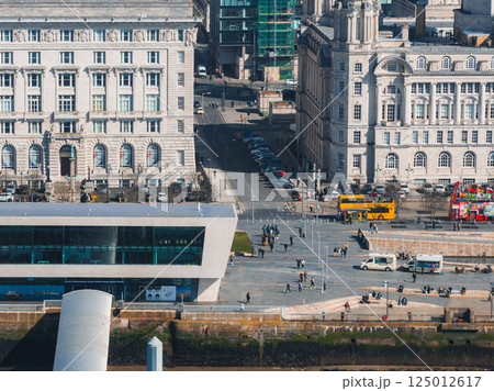 Aerial view of Liverpool showcasing the Three Graces, Museum of Liverpool, waterfront, and vibrant street activity with buses and pedestrians. 125012617