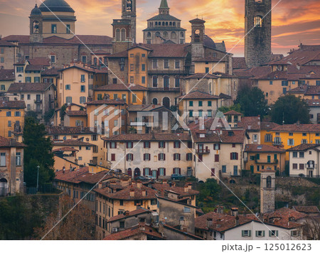 View of Bergamo's old town in Italy during sunset, featuring the Basilica of Santa Maria Maggiore, Campanone bell tower, and terracotta roofed buildings. View of Bergamo's old town in Italy during sunset, featuring the Basilica of Santa Maria Maggiore, Campanone bell tower, and terracotta roofed buildings. 125012623