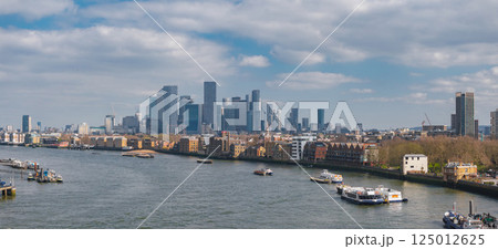 Aerial perspective of London's Canary Wharf skyline with modern skyscrapers, the River Thames with boats, and a mix of historic and modern buildings. Aerial perspective of London's Canary Wharf skyline with modern skyscrapers, the River Thames with boats, and a mix of historic and modern buildings. 125012625