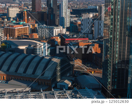 Aerial view of Manchester, UK, showcasing the Manchester Central Convention Complex, modern skyscrapers, and historic brick buildings on a sunny day. 125012630