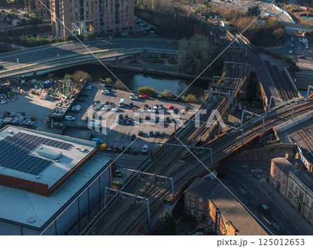 Aerial view of Manchester, UK, showing railway tracks, a parking lot, a waterway, and urban buildings, including a solar paneled modern structure. 125012653