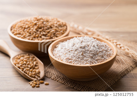 Whole wheat flour with wheat grain in bowl on wooden background Whole wheat flour with wheat grain in bowl on wooden background 125012755