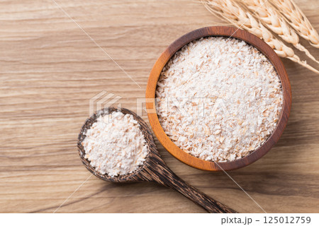 Whole wheat flour in bowl and spoon on wooden background, Table top view Whole wheat flour in bowl and spoon on wooden background, Table top view 125012759