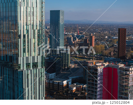 Aerial view of Manchester, UK, on a sunny day with skyscrapers, modern and traditional architecture, construction activity, and suburban areas in the distance. Aerial view of Manchester, UK, on a sunny day with skyscrapers, modern and traditional architecture, construction activity, and suburban areas in the distance. 125012804