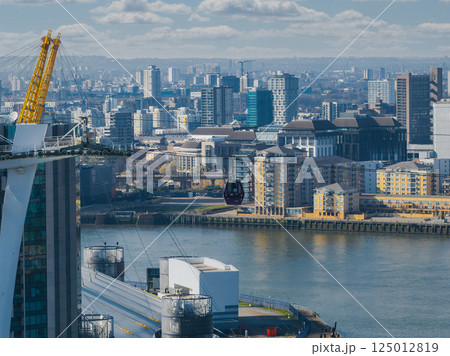 Aerial view of London with the O2 Arena, Emirates Air Line gondola over the River Thames, and modern buildings in Canary Wharf and Greenwich. Aerial view of London with the O2 Arena, Emirates Air Line gondola over the River Thames, and modern buildings in Canary Wharf and Greenwich. 125012819