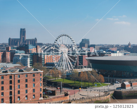Aerial view of Liverpool featuring the Liverpool Cathedral, the Wheel of Liverpool, the MandS Bank Arena, and historic Albert Dock buildings under a clear sky. Aerial view of Liverpool featuring the Liverpool Cathedral, the Wheel of Liverpool, the MandS Bank Arena, and historic Albert Dock buildings under a clear sky. 125012823