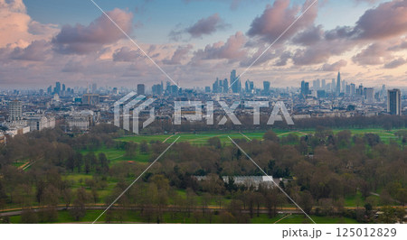 Aerial perspective of London featuring The Shard, City of London skyscrapers, and Hyde Park's green expanse under an overcast sky. 125012829