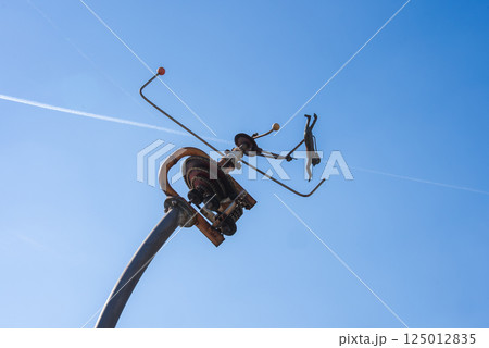A metal sculpture featuring gears, rods, and a human like figure in motion, mounted on a tall pole against a clear blue sky with a contrail. 125012835