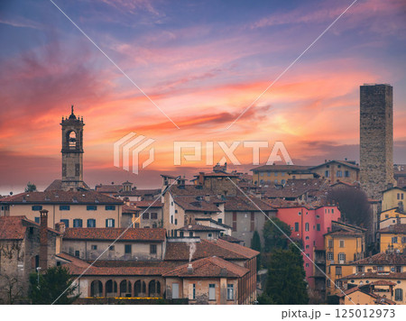 View of Bergamo's old town in Italy during sunset, featuring a medieval tower, a bell tower, terracotta roofs, and colorful historic buildings. View of Bergamo's old town in Italy during sunset, featuring a medieval tower, a bell tower, terracotta roofs, and colorful historic buildings. 125012973