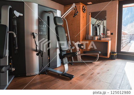 A gym with wooden interiors, Technogym equipment, and a balcony overlooking snow covered peaks in a luxury hotel in the Italian Alps. A gym with wooden interiors, Technogym equipment, and a balcony overlooking snow covered peaks in a luxury hotel in the Italian Alps. 125012980