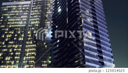Tall modern skyscraper illuminated at night in an urban environment Tall modern skyscraper illuminated at night in an urban environment 125014025