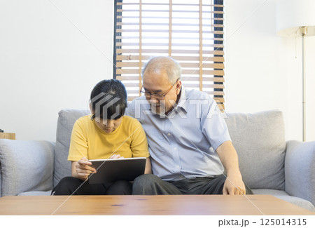Old senior asian grandparent play and watch computer tablet with grandchildren girl at home. Bonding relationship in family.  125014315