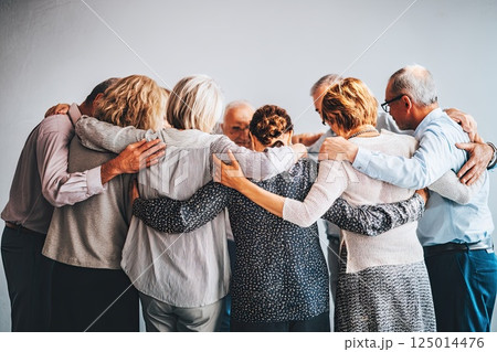 Group therapy and support - middle aged men and women hug, supporting each other during psychological practice. A supportive embrace speaks volumes during group therapy sessions. 125014476