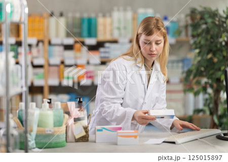 Female pharmacist working at computer offering ointment Female pharmacist working at computer offering ointment 125015897