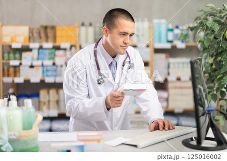 Male pharmacist checking information about medicine on computer Male pharmacist checking information about medicine on computer 125016002