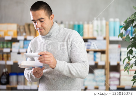 Young man chooses ointment at pharmacy 125016378