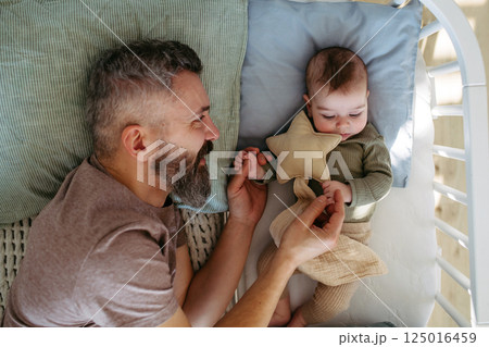 Father putting the baby to sleep, lying next to him in the crib. Father putting the baby to sleep, lying next to him in the crib. 125016459
