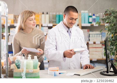 Man pharmacist is working at computer, communicate with girl customer 125016462