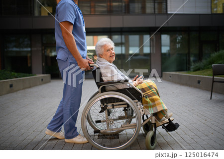 Side view of caregiver pushing senior woman in wheelchair. 125016474