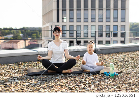 Woman and young girl practicing meditation outdoors on urban rooftop, expressing mindfulness and tranquility. Woman and young girl practicing meditation outdoors on urban rooftop, expressing mindfulness and tranquility. 125016651