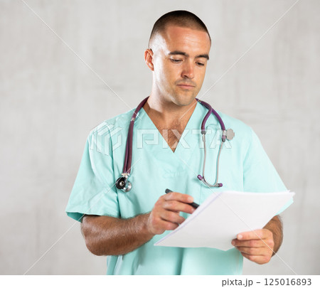 Portrait of male doctor in medical gown with stethoscope making notes in patient medical history Portrait of male doctor in medical gown with stethoscope making notes in patient medical history 125016893