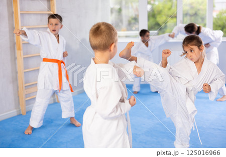 Karate kids in kimono sparring together during their group karate training in gym Karate kids in kimono sparring together during their group karate training in gym 125016966