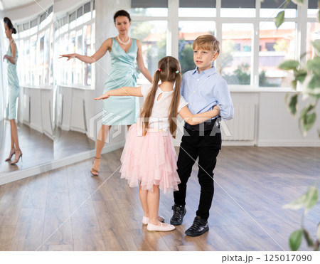 Couple of preteen dancers rehearsing ballroom dance while female teacher 125017090