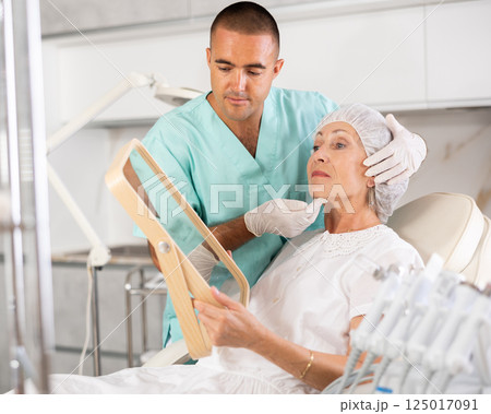 Man beautician examining face skin of female patient after cosmetology procedure in clinic Man beautician examining face skin of female patient after cosmetology procedure in clinic 125017091