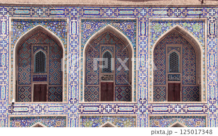 Famous landmark - Ulugh Beg Madrasah on Registan square, Samarkand, Uzbekistan. Arches with tile ornament in the courtyard of Ulugh Beg Madrasa. Text on the wall is a quote from the Quran 125017348