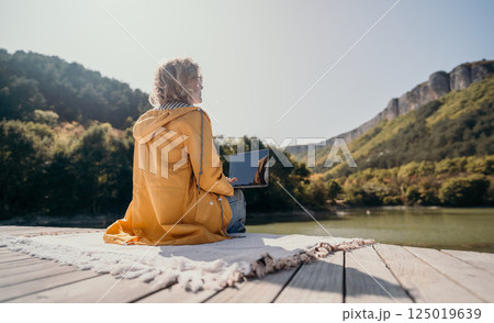 Woman Relaxing with a Laptop on a Wooden Dock by a Lake 125019639