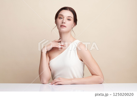 A beautiful young woman with clean, fresh skin against a beige background. Skincare, facial treatment, cosmetology, beauty, and spa. An elegant portrait of an woman. 125020020