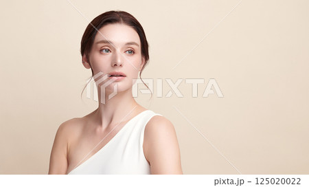 A beautiful young woman with clean, fresh skin against a beige background. Skincare, facial treatment, cosmetology, beauty, and spa. An elegant portrait of an woman. 125020022
