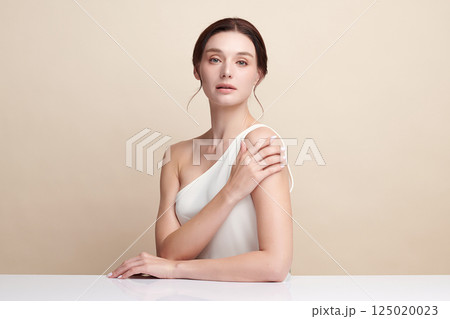 A beautiful young woman with clean, fresh skin against a beige background. Skincare, facial treatment, cosmetology, beauty, and spa. An elegant portrait of an woman. 125020023