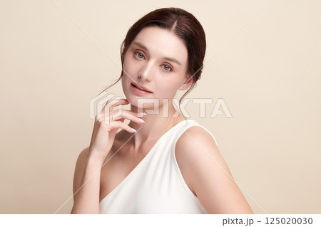 A beautiful young woman with clean, fresh skin against a beige background. Skincare, facial treatment, cosmetology, beauty, and spa. An elegant portrait of an woman. 125020030