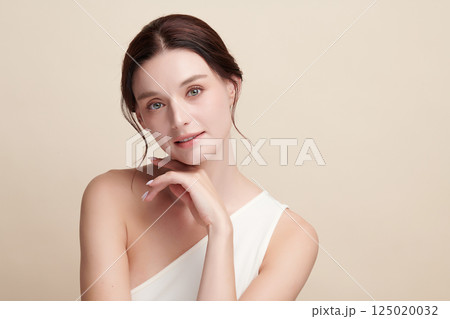 A beautiful young woman with clean, fresh skin against a beige background. Skincare, facial treatment, cosmetology, beauty, and spa. An elegant portrait of an woman. 125020032