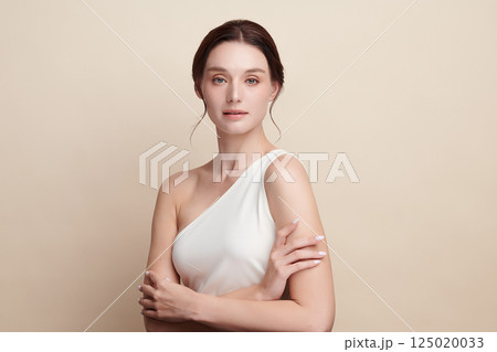 A beautiful young woman with clean, fresh skin against a beige background. Skincare, facial treatment, cosmetology, beauty, and spa. An elegant portrait of an woman. 125020033