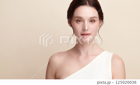A beautiful young woman with clean, fresh skin against a beige background. Skincare, facial treatment, cosmetology, beauty, and spa. An elegant portrait of an woman. 125020036
