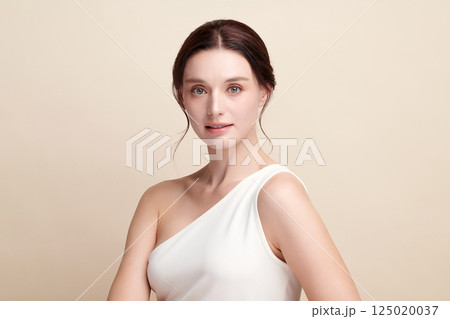A beautiful young woman with clean, fresh skin against a beige background. Skincare, facial treatment, cosmetology, beauty, and spa. An elegant portrait of an woman. 125020037