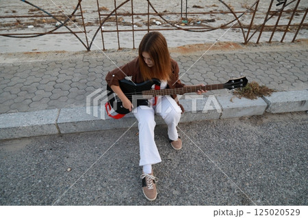 Girl Plays The Bass Instrument Sitting On The Step Near The Street At Evening 125020529
