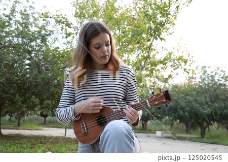 Girl Strums With Ukulele Musical Instrument Near A Tree In The Mountains Girl Strums With Ukulele Musical Instrument Near A Tree In The Mountains 125020545