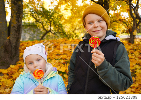 Portrait of a boy and a girl eating lollipops in an autumn park. Portrait of a boy and a girl eating lollipops in an autumn park. 125021809