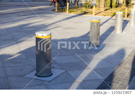 Retractable stainless steel bollards on paved plaza casting long shadows in morning sunlight Retractable stainless steel bollards on paved plaza casting long shadows in morning sunlight 125021907