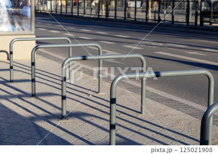 Empty metal bike racks casting long shadows on sunlit sidewalk beside city road and crosswalk Empty metal bike racks casting long shadows on sunlit sidewalk beside city road and crosswalk 125021908