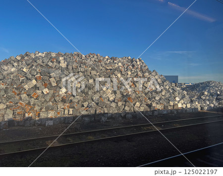 Large pile of compressed metal cubes stacked at industrial recycling site near railway tracks under clear blue sky in sunlight Large pile of compressed metal cubes stacked at industrial recycling site near railway tracks under clear blue sky in sunlight 125022197