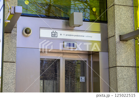 Modern glass elevator entrance to underground pedestrian subway with sign and surveillance camera on urban street 125022515
