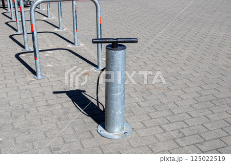 Metal bicycle air pump with hose installed on paved sidewalk near bike rack on sunny day in urban outdoor environment Metal bicycle air pump with hose installed on paved sidewalk near bike rack on sunny day in urban outdoor environment 125022519