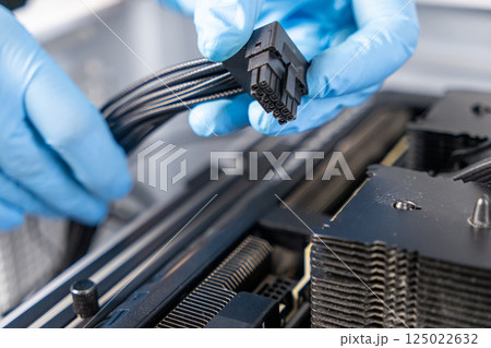 Technician in blue gloves holding 16-pin GPU power cable above graphics card inside custom-built desktop PC during installation process Technician in blue gloves holding 16-pin GPU power cable above graphics card inside custom-built desktop PC during installation process 125022632