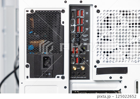 Close-up of back panel of white computer case showing power supply, motherboard I/O ports, and ventilation grid with USB, HDMI, and audio connectors 125022652
