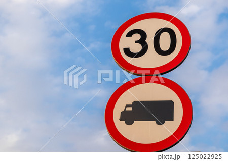 Traffic signs showing speed limit of 30 kilometers per hour and truck restriction against cloudy blue sky background 125022925